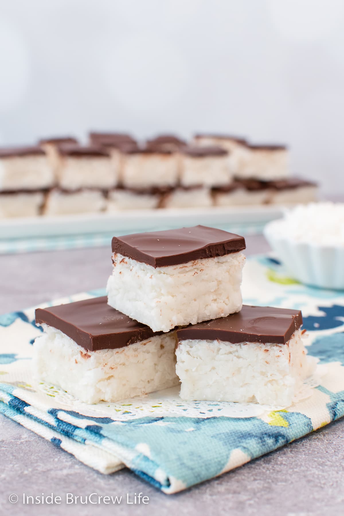 Three coconut fudge squares stacked on a blue towel.