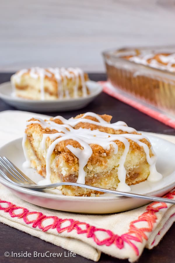 A white plate with square of sour cream coffee cake with glaze on it.