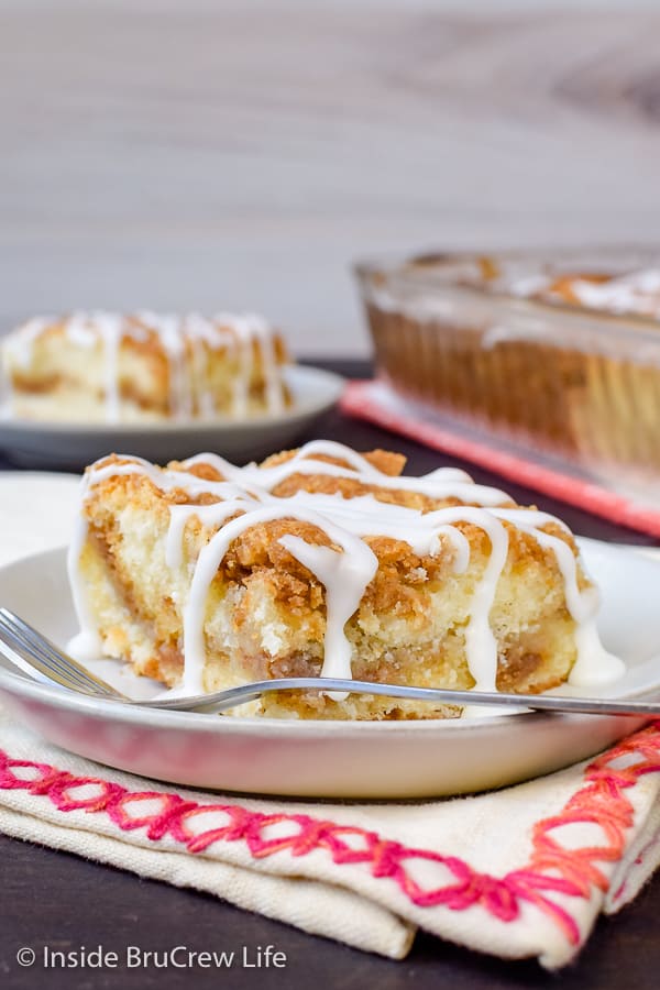 A white plate with a slice of classic coffee cake with glaze on it and more cake behind it.