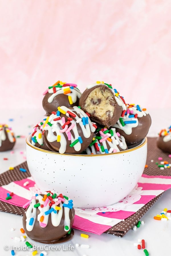 A white bowl filled with chocolate covered cookie dough bites. 