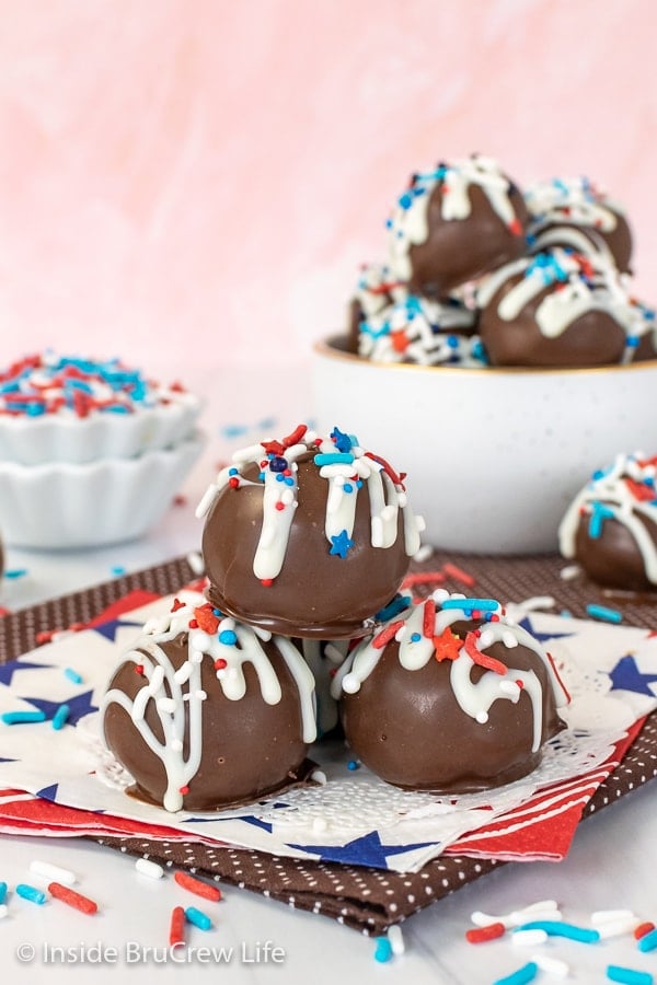 Four cookie dough truffles dipped in chocolate and decorated with red white and blue sprinkles stacked on a white napkin