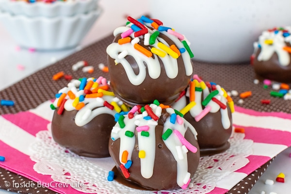 Four chocolate chip cookie dough truffles dipped in chocolate and decorated with white chocolate and sprinkles on a pink and white napkin