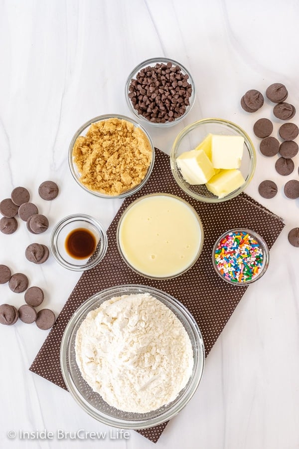 Bowls of ingredients to make cookie dough truffles on a white board.