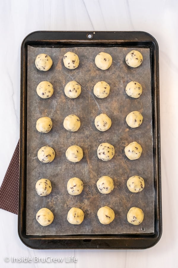 A cookie tray with wax paper and cookie dough truffles lined up on it