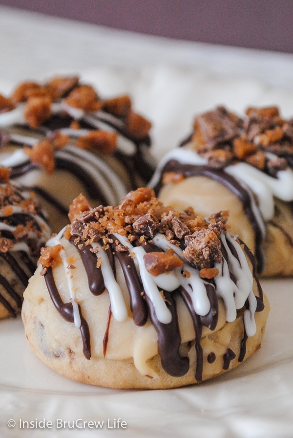 A white plate with toffee cookies on it that have chocolate drizzles and toffee candy on top.