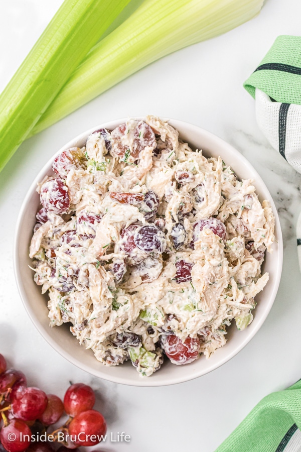 A white board with a white bowl full of grape pecan chicken salad.