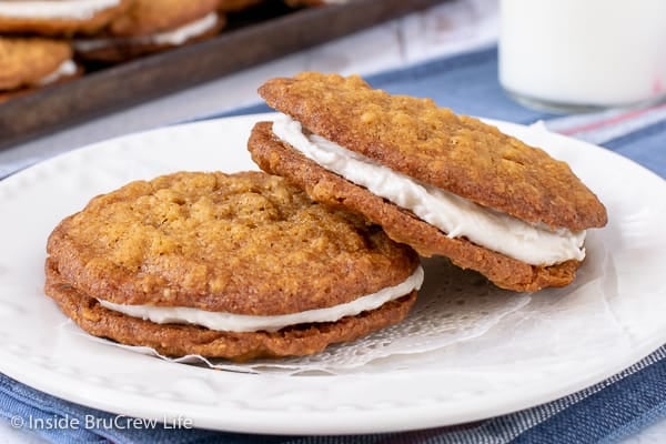 A white plate with two homemade oatmeal creme pies filled with marshmallow frosting on it.