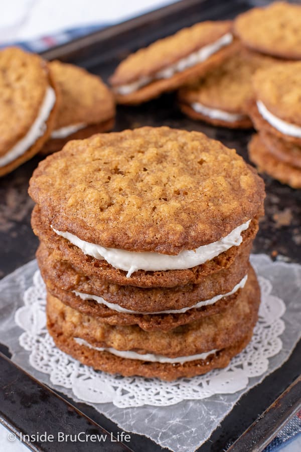 A metal tray with a stack of homemade oatmeal creme pies on it and more behind it.