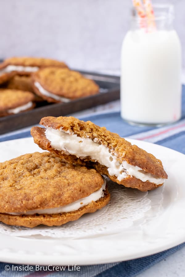 A white plate with two oatmeal cream pies on it with a bite out of one showing the marshmallow creme filling.
