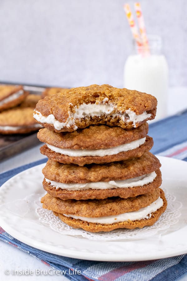 Oatmeal Cream Pie cookies stacked on a white plate with a glass of milk behind it.