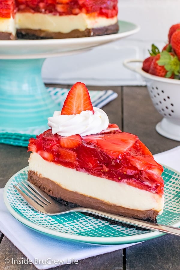 A white and teal plate with a slice of strawberry chocolate cheesecake and a fork on it