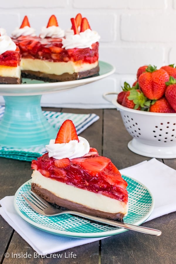 A slice of strawberry chocolate cheesecake on a teal and white plate with the full cheesecake behind it