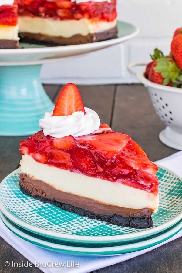 A slice of strawberry chocolate cheesecake topped with whipped cream and a strawberry on a teal and white plate