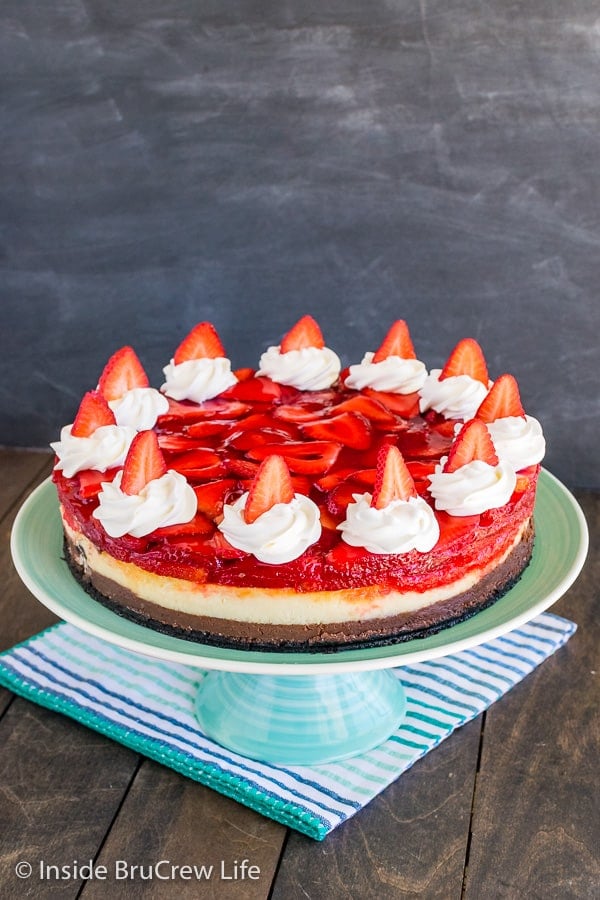 A whole strawberry chocolate cheesecake topped with whipped cream swirls and strawberries on a light green cake plate