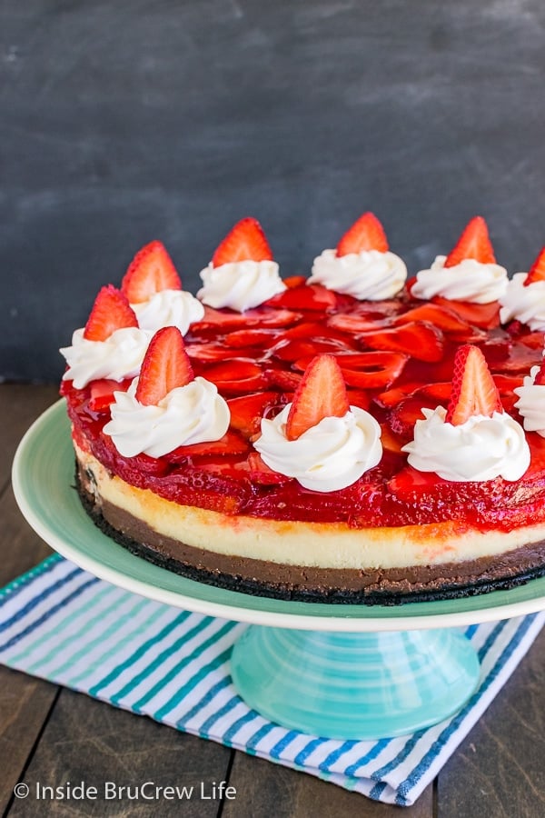 A close up of the side of a full Strawberry Chocolate Cheesecake topped with whipped cream and strawberries