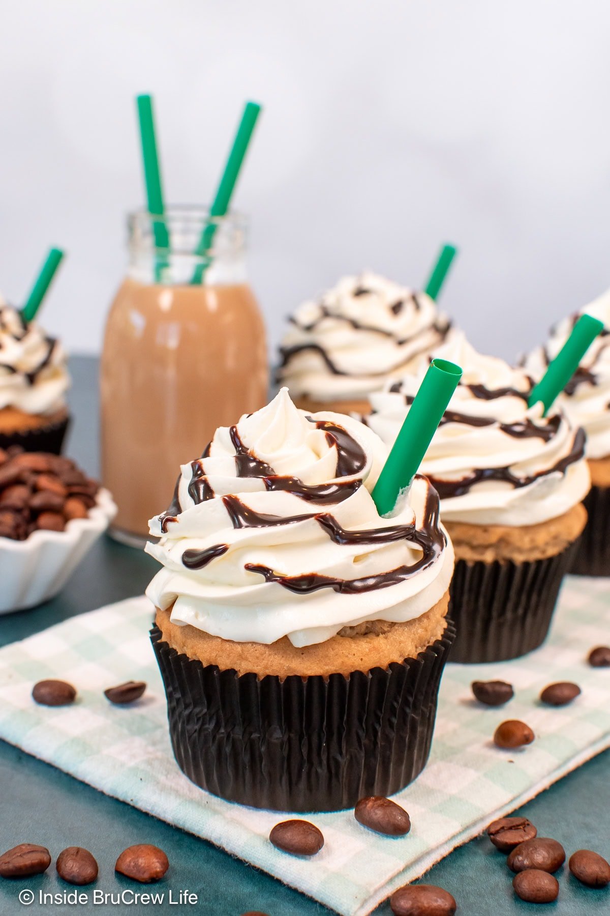 Frosted white chocolate mocha frappuccino cupcakes on a checkered towel.