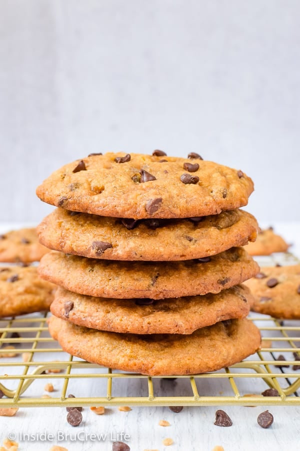 Four banana chocolate chip cookies stacked on a wire rack with more cookies behind it