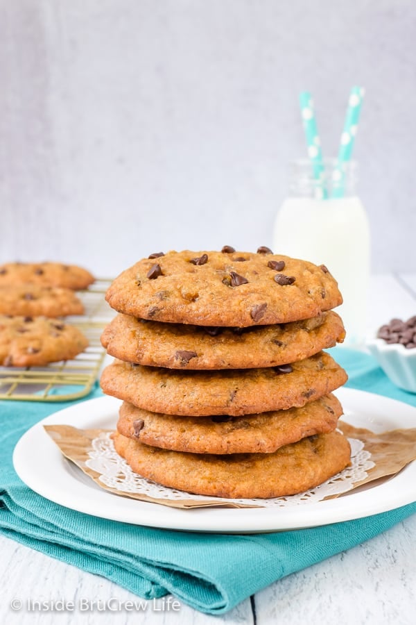 A white plate with a stack of banana chocolate chip cookies on it and a glass of milk behind it