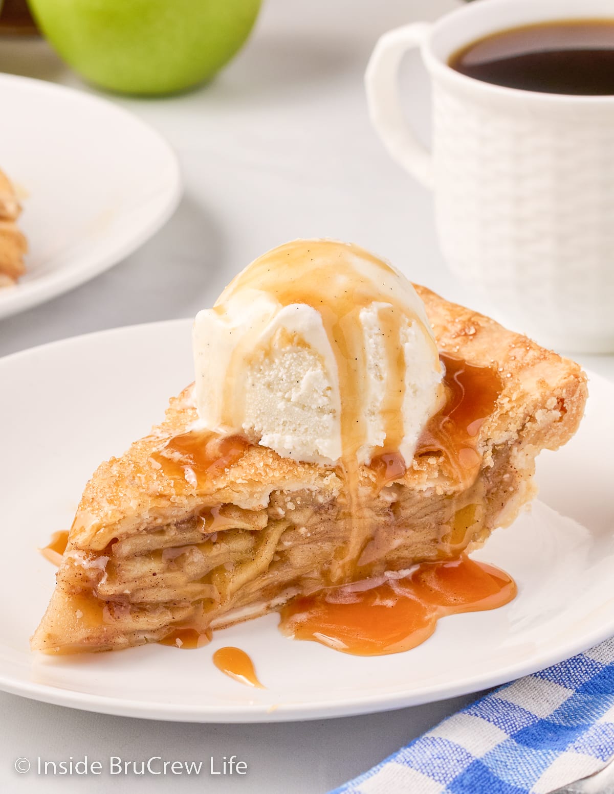 A slice of apple pie topped with vanilla ice cream and caramel on a white plate.