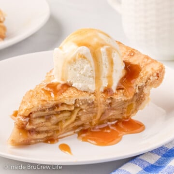 An apple pie slice topped with vanilla ice cream and caramel topping.