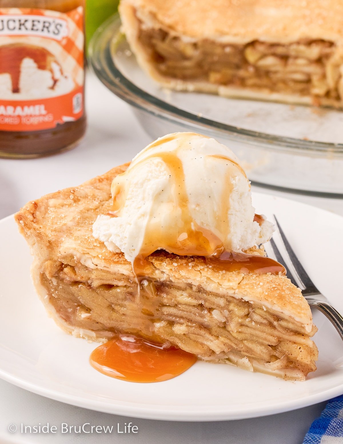 A white plate with a slice of apple pie topped with ice cream and caramel.