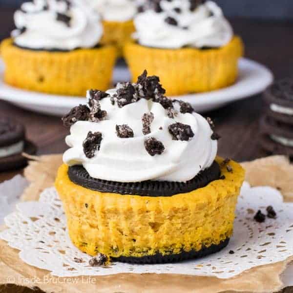 A pumpkin Oreo cheesecake topped with cool whip and cookie crumbles on a white doily