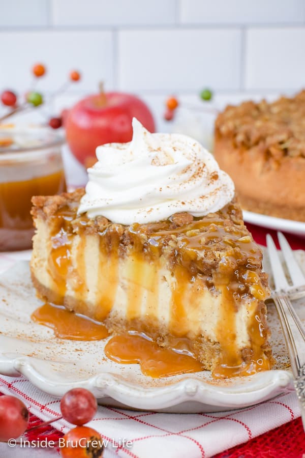 A slice of apple cheesecake topped with crisp topping, caramel, and whipped cream.