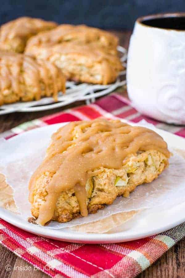 A white plate with a caramel apple scone on it and more scones behind it