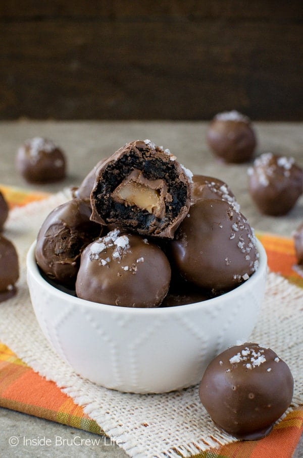 A white bowl with salted caramel brownie bites in it and a bite take out of the very top brownie bite