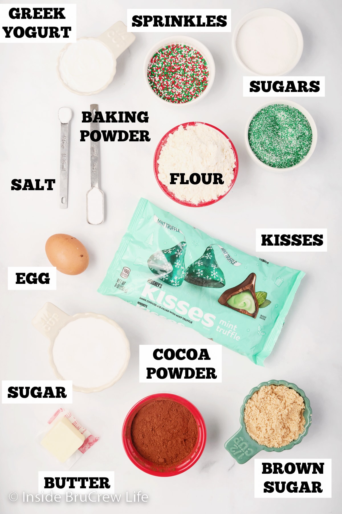 A white board with bowls of ingredients for chocolate kiss cookies.