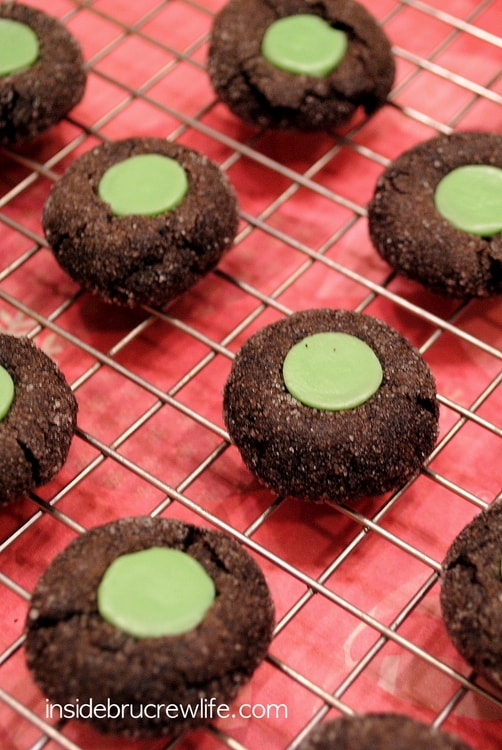 Chocolate cookies rolled in sugar with a green candy in them on a cooling rack.