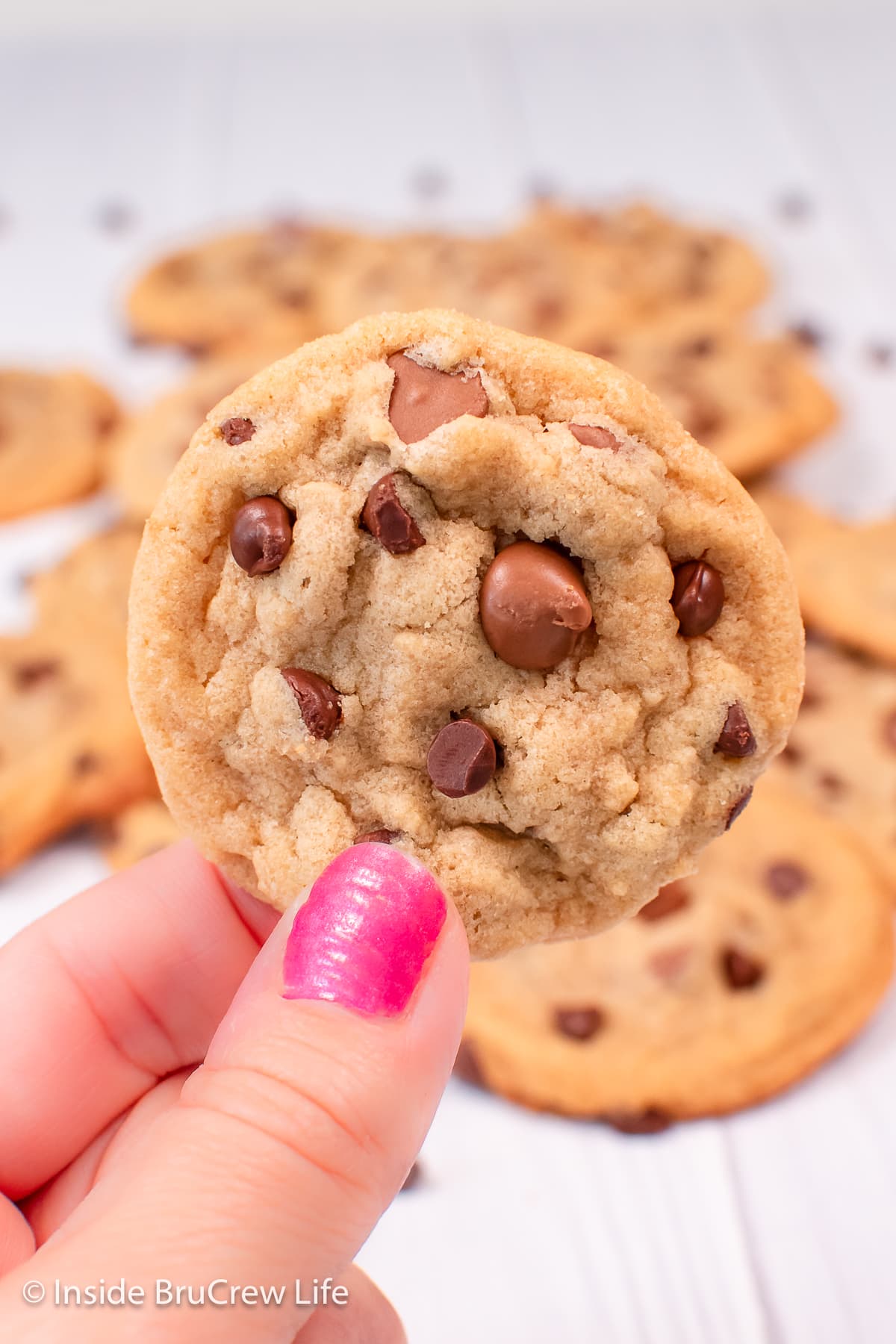 A hand holding up a chocolate chip cookie.