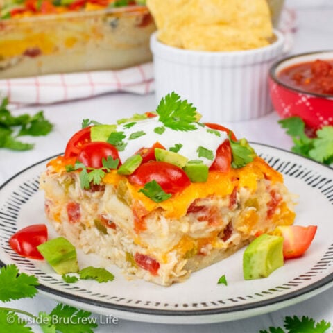 A square of chicken ole casserole topped with tomatoes, avocados, and sour cream on a white plate.