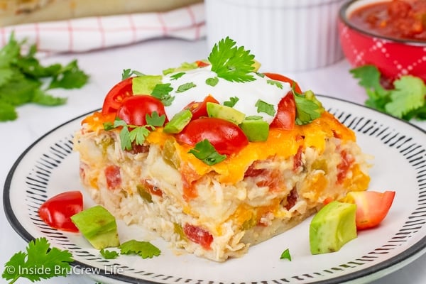 A white plate with chicken ole topped with sour cream, tomatoes, avocados, and cilantro.