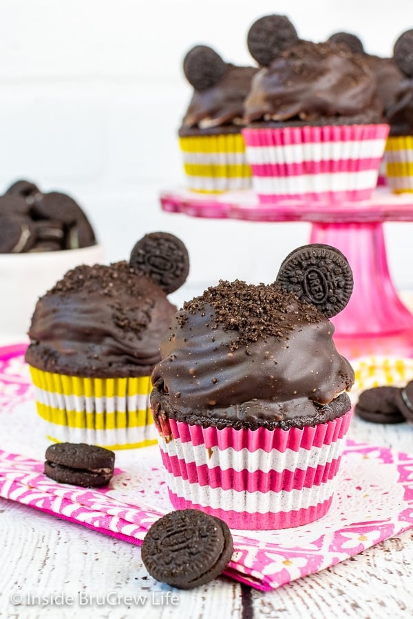 Two chocolate cookies and cream cupcakes topped with Oreo frosting, chocolate frosting, and an Oreo cookie on a pink towel