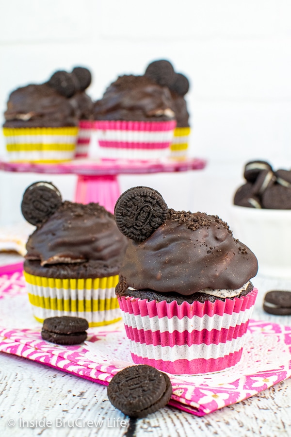 Two chocolate cookies and cream cupcakes topped with Oreo frosting, chocolate frosting, and a cookie on a pink towel