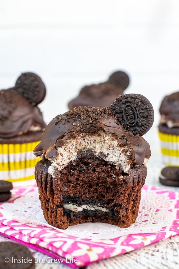 Four cookies and cream cupcakes topped with Oreo frosting, chocolate frosting, and Oreo cookies on a white board with a bite out of the front cupcake