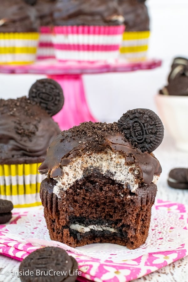 Two cookies and cream cupcakes topped with Oreo frosting and chocolate frosting with a bite out of one showing the hidden cookie