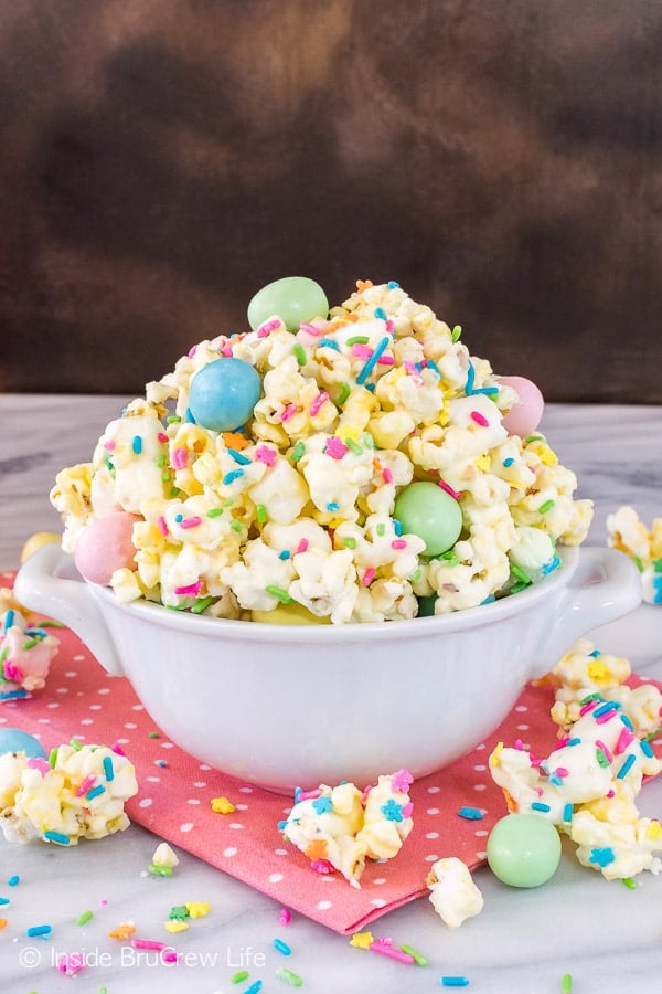 White chocolate covered popcorn in a white bowl on top of a pink towel.