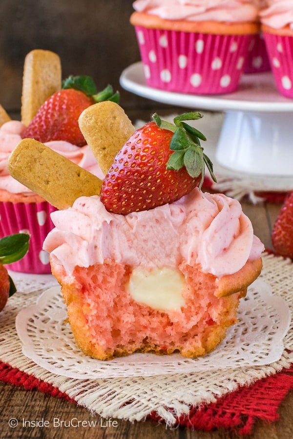 A strawberry cheesecake cupcake with a bite taken out of it showing the hidden filling.