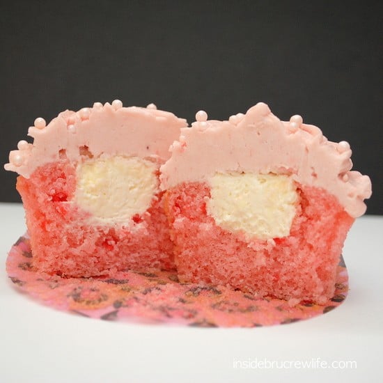 A strawberry cupcake with strawberry buttercream cut in half showing the no bake cheesecake center. 