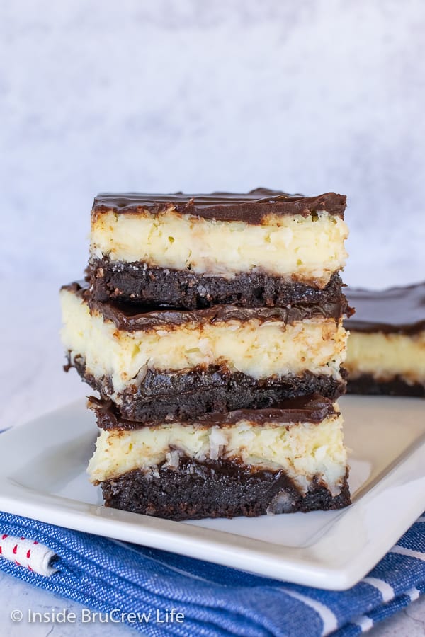 A stack of three Coconut Cream Cheesecake Brownies on a white plate with a blue towel under it