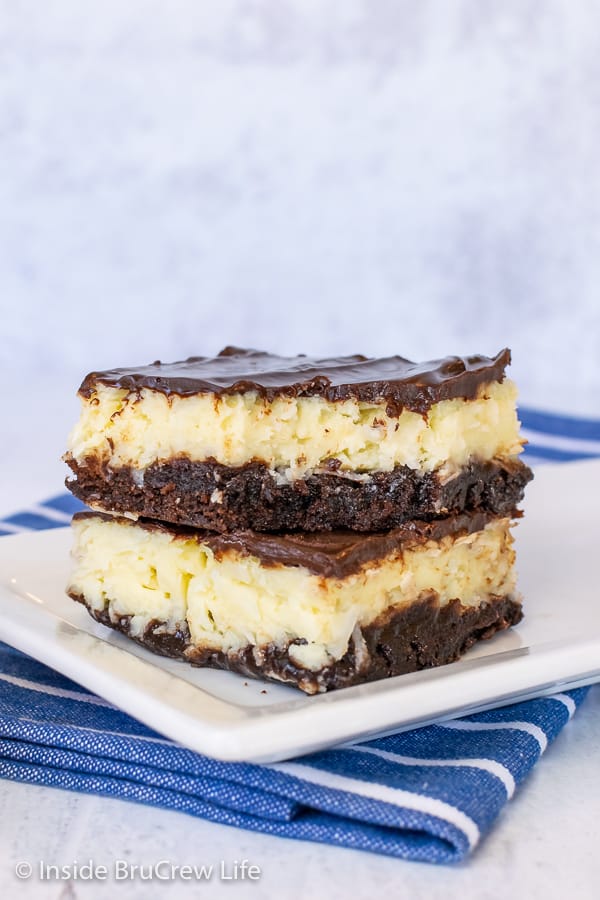 Two squares of coconut cream cheesecake brownies stacked on top of each other on a white plate