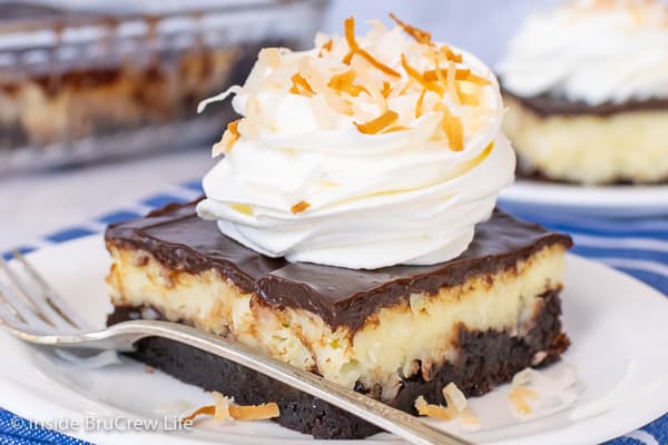 A square of Coconut Cream Cheesecake Brownies topped with Cool Whip and toasted coconut on a white plate 