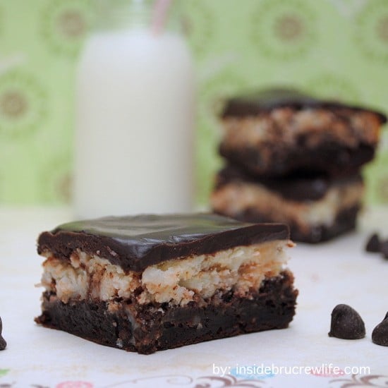 A square of coconut cream cheesecake brownies on a white paper with more behind it