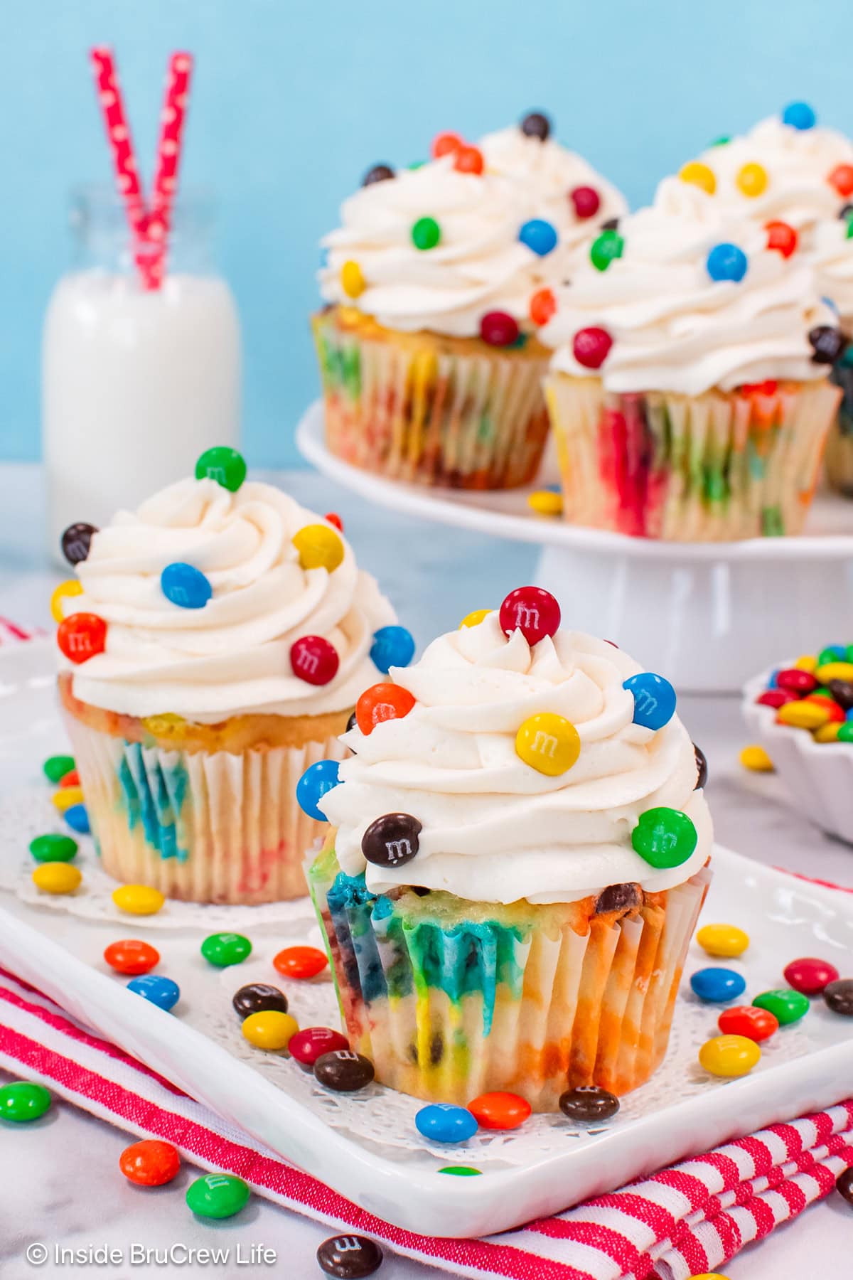 Two vanilla cupcakes on a plate with colorful candies on top.