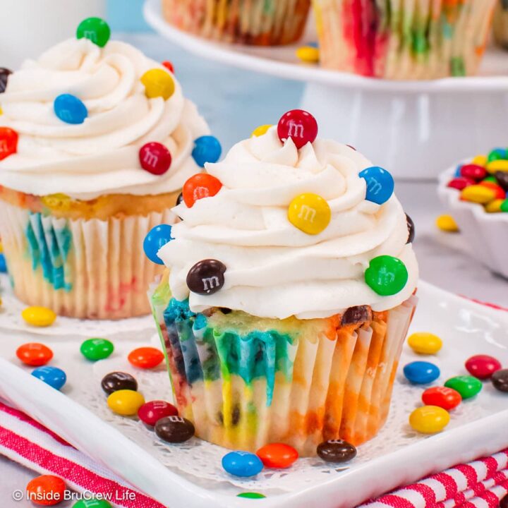 Two vanilla cupcakes on a plate with colorful candies on top.
