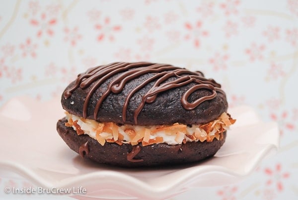 A pink plate with a chocolate whoopie pie filled with coconut frosting on it.