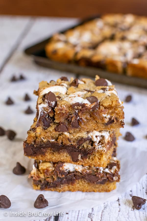 A stack of three Peanut Butter S'mores Blondies on a piece of parchment with chocolate chips around it