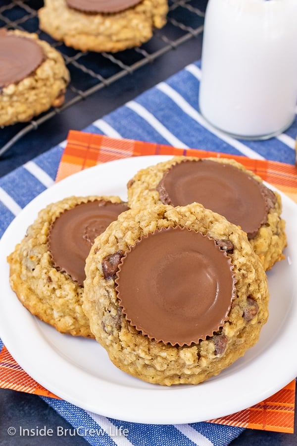 A white plate with three oatmeal chocolate chip banana cookies topped with peanut butter cups on it